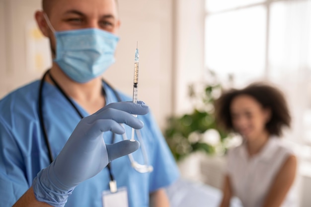 Doctor sosteniendo una jeringa con vacuna junto a un paciente