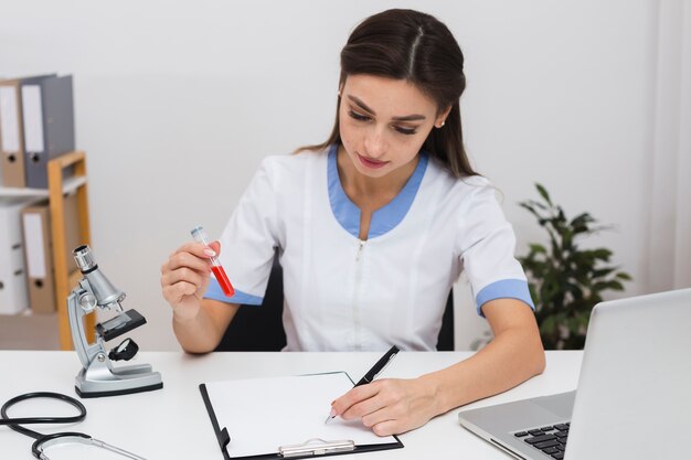 Doctor sosteniendo una muestra de sangre y escribiendo un informe