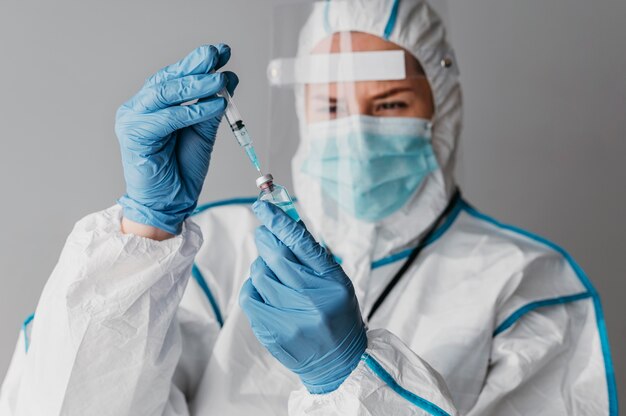 Doctor sosteniendo preparando una vacuna mientras usa equipo de protección
