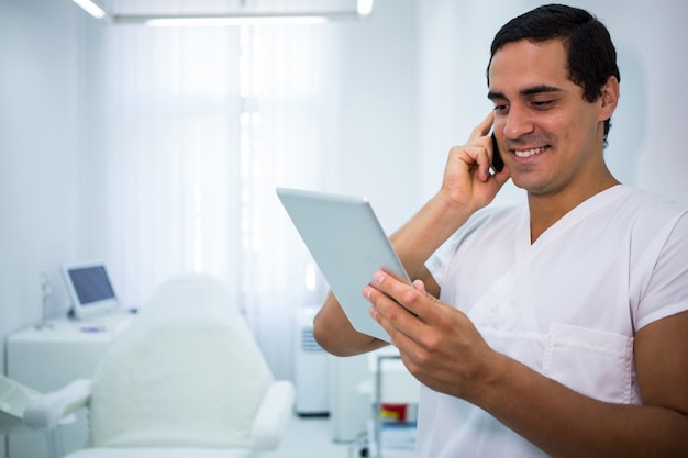 Doctor sosteniendo una tableta digital mientras habla por teléfono móvil
