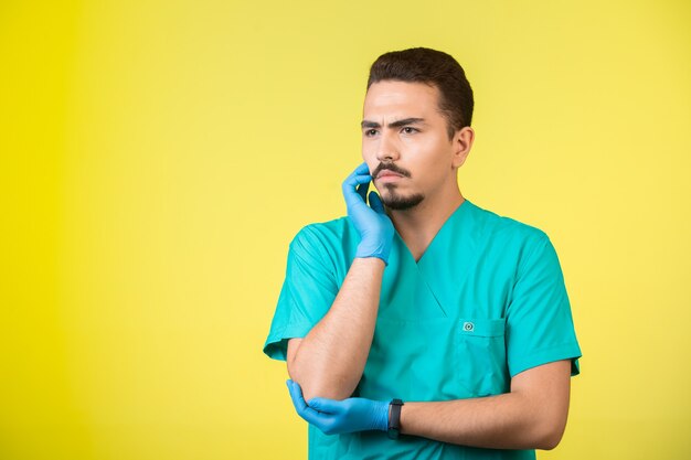 Doctor en uniforme y máscara de mano mirando y tratando de recordar.