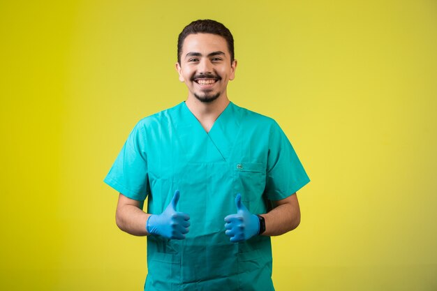 Doctor en uniforme y máscara de mano satisfecho y sonriente, de pie en el medio.