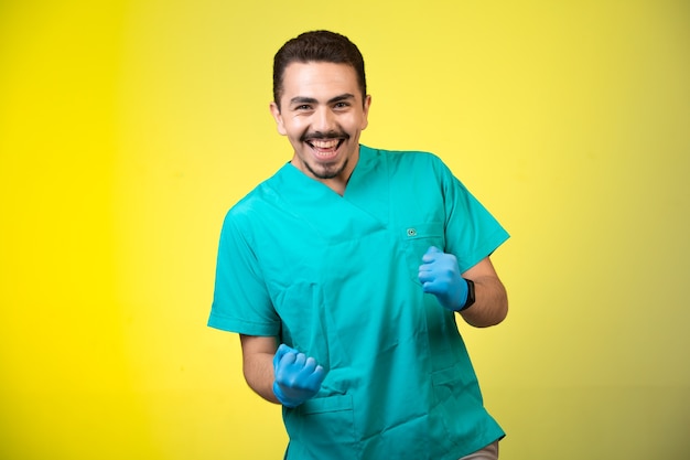 Doctor en uniforme verde y máscara de mano sonriendo y mostrando su felicidad en amarillo.