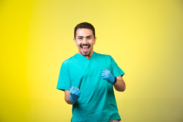 Doctor en uniforme verde y máscara de mano sonriendo y mostrando su felicidad.