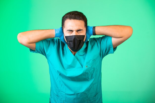 Doctor en uniforme verde y mascarilla cubriendo sus oídos.