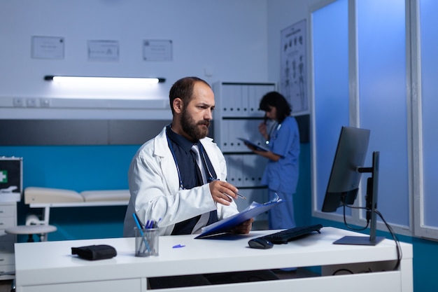 Doctor usando computadora y archivos de chequeo para trabajos de salud