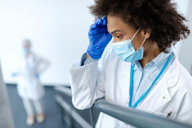 Doctora afroamericana angustiada con mascarilla protectora en el pasillo del hospital