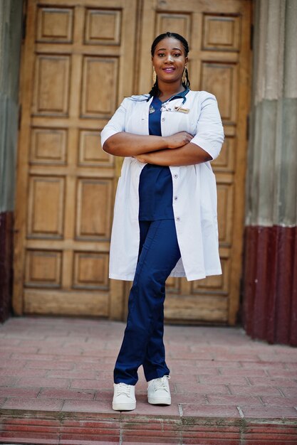 Doctora afroamericana en bata de laboratorio con estetoscopio al aire libre contra la puerta de la clínica