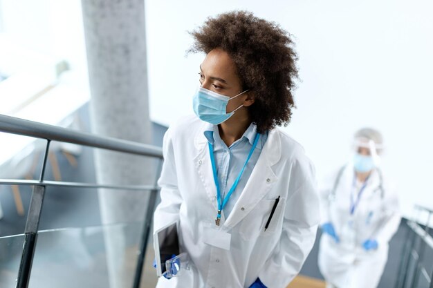 Doctora afroamericana con mascarilla subiendo las escaleras y mirando hacia otro lado