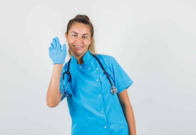 Doctora agitando la mano para saludar en uniforme azul