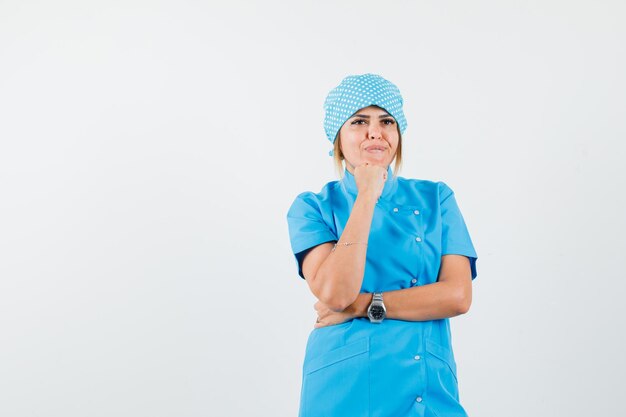 Doctora apoyando la barbilla en el puño levantado en uniforme azul y luciendo sensato