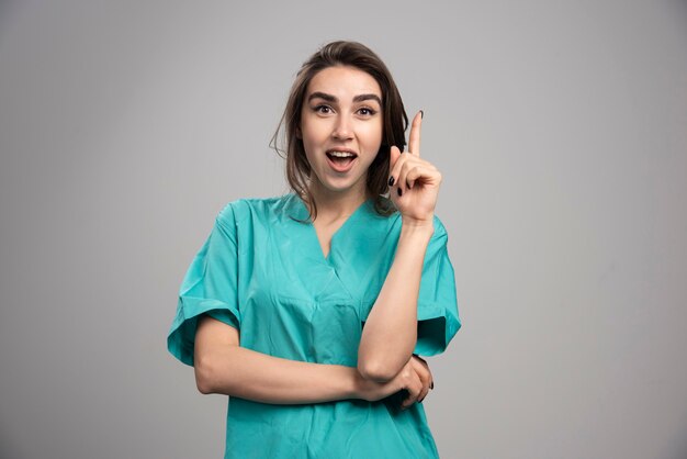 Doctora apuntando hacia arriba sobre fondo gris. Foto de alta calidad