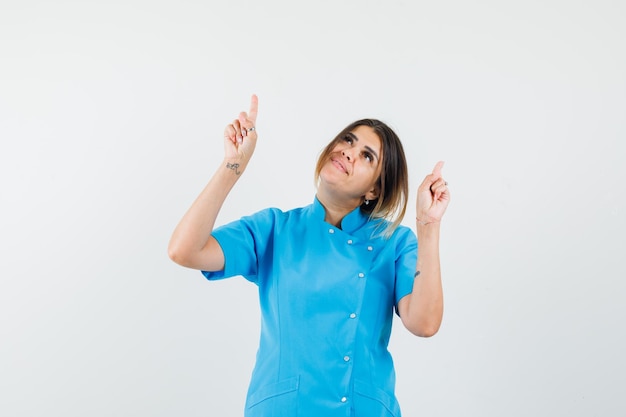 Doctora apuntando hacia arriba en uniforme azul y mirando alegre