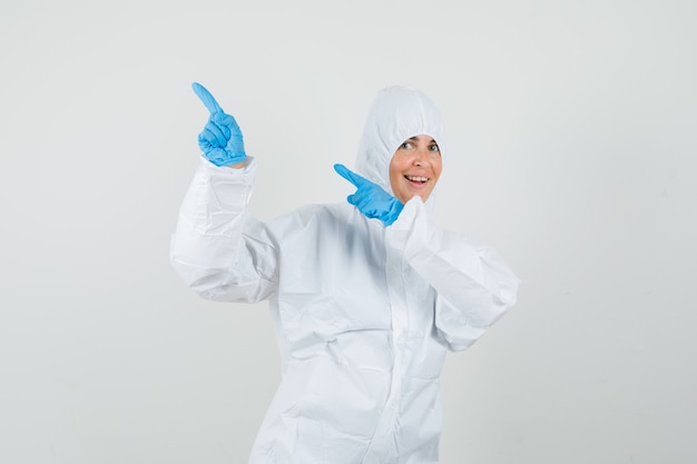 Doctora apuntando hacia el lado con los dedos hacia arriba en traje protector