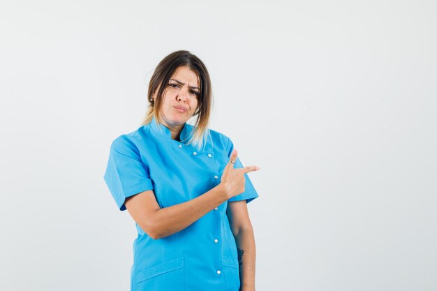 Doctora apuntando hacia el lado mientras fruncía el ceño en uniforme azul