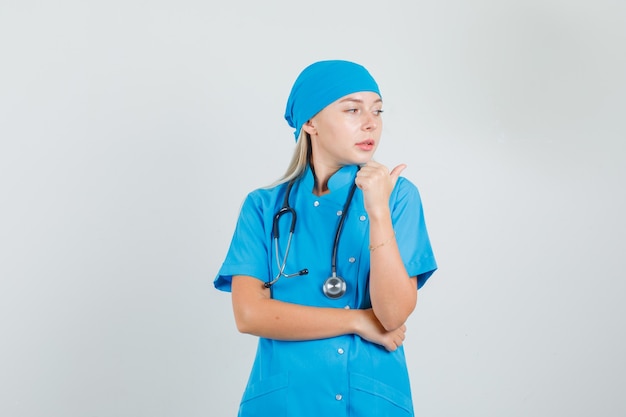 Doctora apuntando hacia el lado con el pulgar en uniforme azul y luciendo lindo