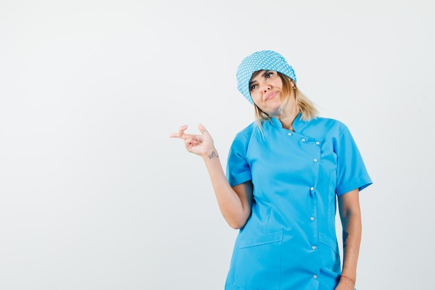 Doctora apuntando hacia el lado en uniforme azul y mirando soñadora