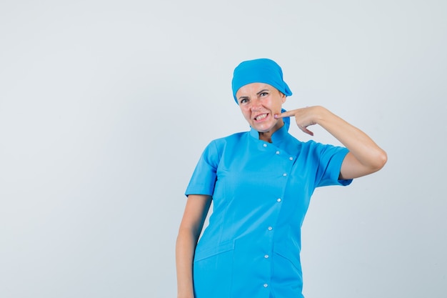 Doctora apuntando a su barbilla en vista frontal uniforme azul.