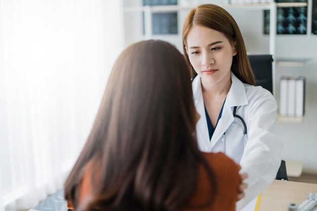 Una doctora asiática alienta y apoya a la paciente cansora después de consultar y examinar en el concepto de ideas de salud del hospital clínico