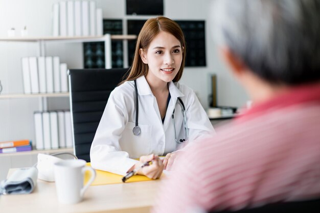 Una doctora asiática inteligente y atractiva explica y discute con un anciano asiático para consultar el concepto de salud de fondo de la clínica