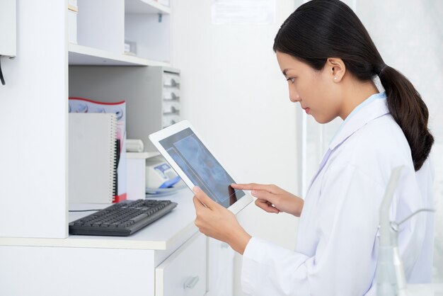 Doctora asiática mirando la radiografía del cráneo del paciente en tableta en la oficina