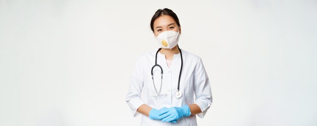 Doctora asiática sonriente con máscara médica de respirador y guantes de goma listos para ayudar a pararse en c