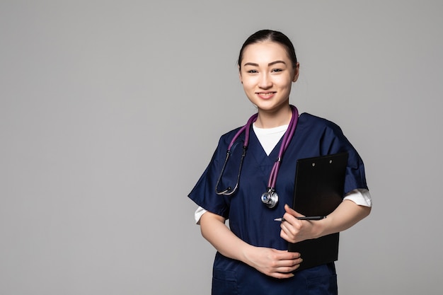 Doctora asiática sosteniendo la pluma escribiendo algo en el portapapeles en la pared blanca