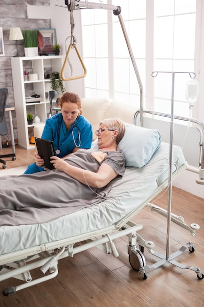 Foto gratuita doctora ayudando a una anciana en un hogar de ancianos a usar wifi en una tableta.