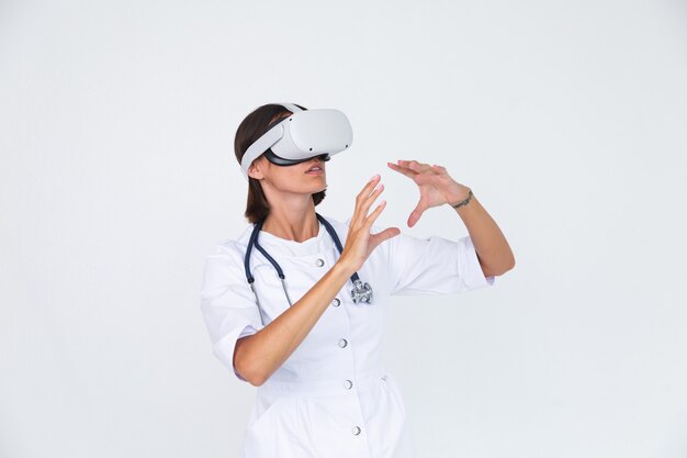 Doctora en bata de laboratorio en blanco aislado, con gafas de realidad virtual toque el aire