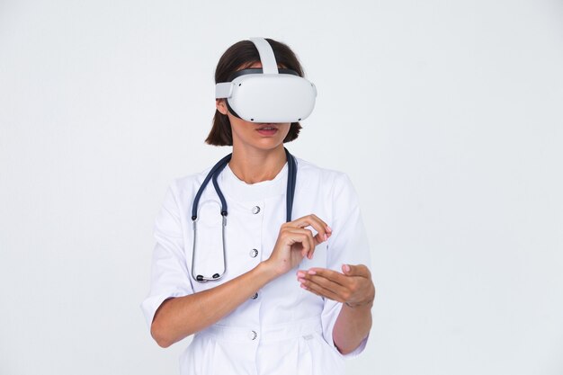 Doctora en bata de laboratorio en blanco aislado, con gafas de realidad virtual toque el aire