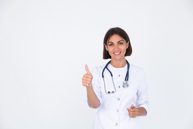 Doctora en bata de laboratorio en blanco aislado, sonrisa confiada mostrar pulgar hacia arriba