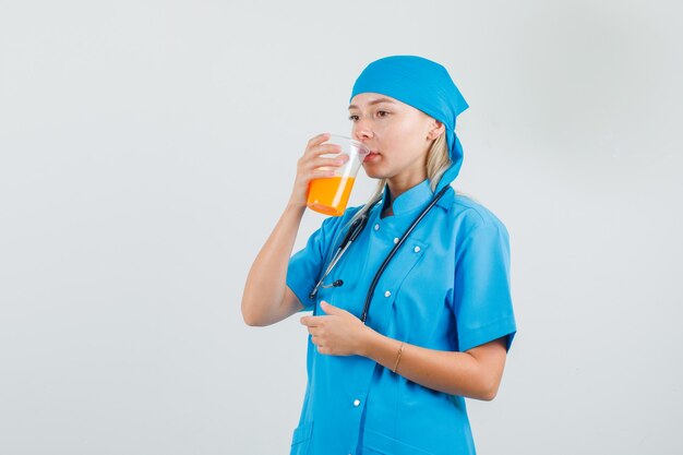 Doctora bebiendo jugo de frutas mientras piensa en uniforme azul