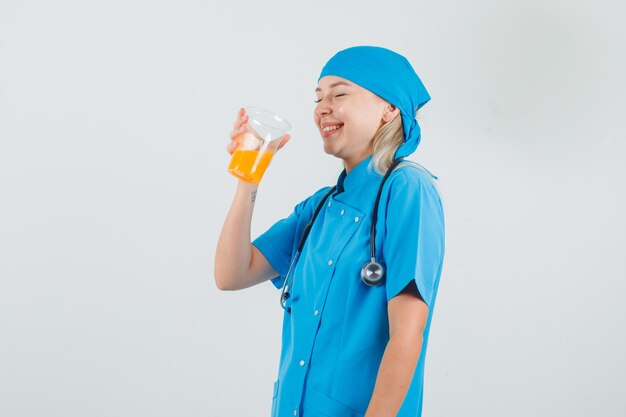 Doctora bebiendo jugo de frutas y riendo en uniforme azul