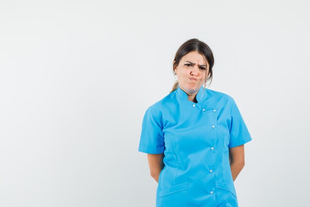 Doctora con el ceño fruncido en uniforme azul y mirando disgustado