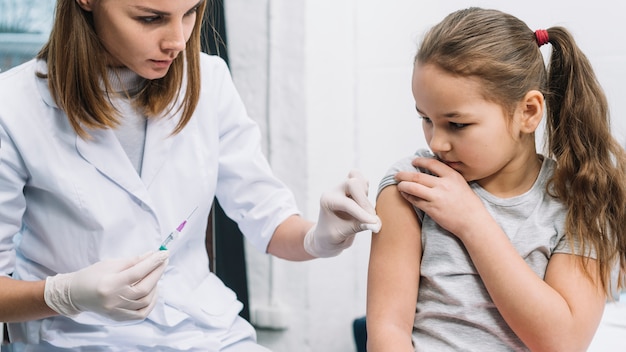 Doctora dando jeringa en brazo de niña enferma