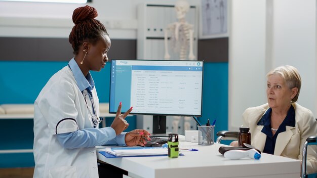 Doctora dando papel de prescripción a una mujer con discapacidad, ayudando con la medicación y el tratamiento en la visita de control. Médico que consulta a un paciente anciano en silla de ruedas con discapacidad.