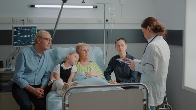 Doctora discutiendo sobre el tratamiento y la medicina con el paciente y la familia en la sala del hospital. Niño, madre y hombre hablando con un médico sobre diagnóstico y recuperación, dando apoyo a una mujer enferma.