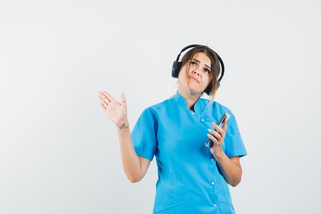 Doctora disfrutando de la música con auriculares, sosteniendo el teléfono móvil en uniforme azul