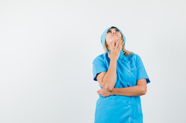 Foto gratuita doctora doblando la cabeza hacia atrás en uniforme azul y mirando soñadora