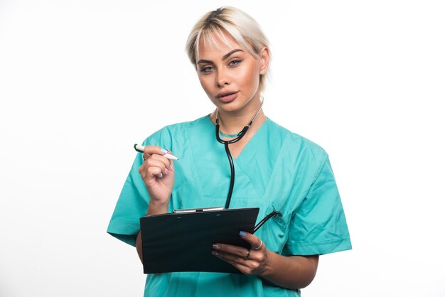 Doctora escribiendo algo en el portapapeles con lápiz en la pared blanca.