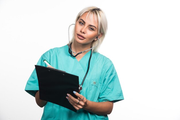 Doctora escribiendo algo en el portapapeles sobre fondo blanco. Foto de alta calidad