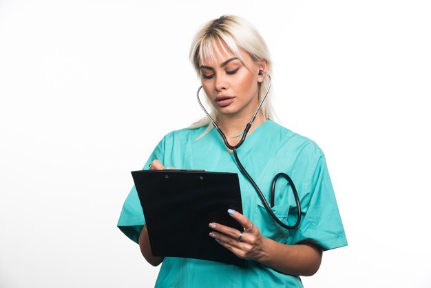 Doctora escribiendo algo en el portapapeles sobre fondo blanco. Foto de alta calidad