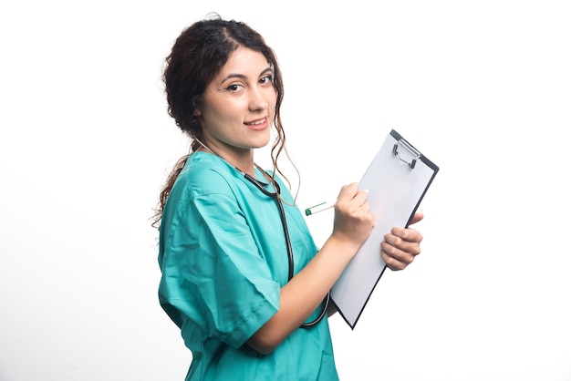 Doctora con estetoscopio escribe algo en un portapapeles sobre fondo blanco. Foto de alta calidad