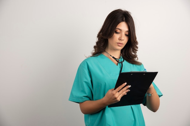 Doctora con estetoscopio escribiendo en el portapapeles con cuidado.