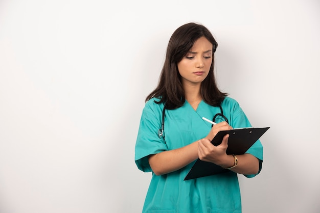 Doctora con estetoscopio escribiendo en un portapapeles. Foto de alta calidad