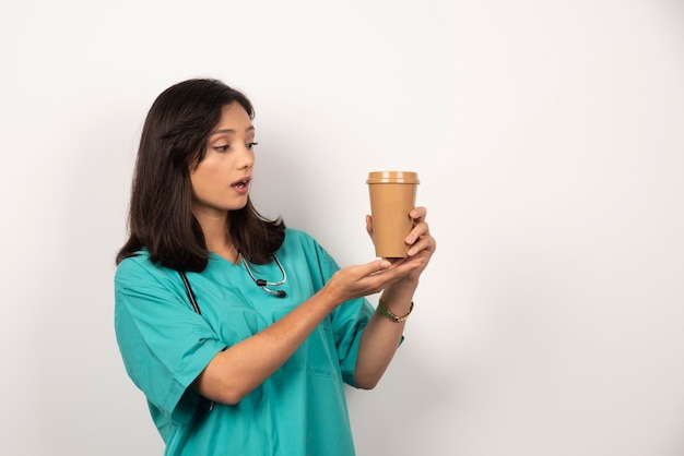 Doctora con estetoscopio mirando café sobre fondo blanco. Foto de alta calidad