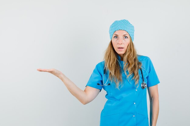 Doctora extendiendo la palma a un lado en uniforme azul y mirando perplejo