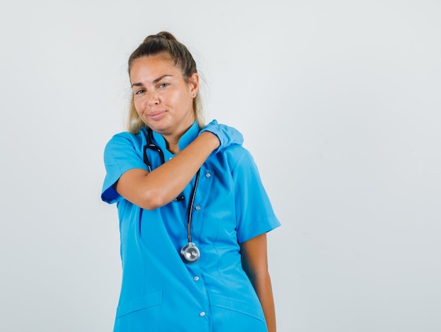 Doctora frotándose el hombro para relajarse en uniforme azul