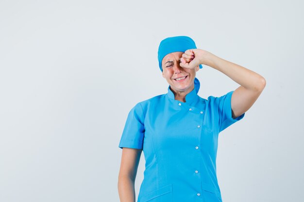 Doctora frotándose los ojos mientras llora en uniforme azul y parece ofendida. vista frontal.