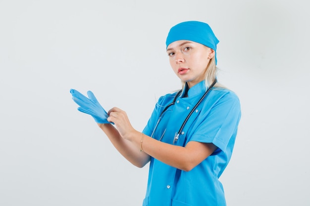 Doctora con guantes médicos en uniforme azul y aspecto serio